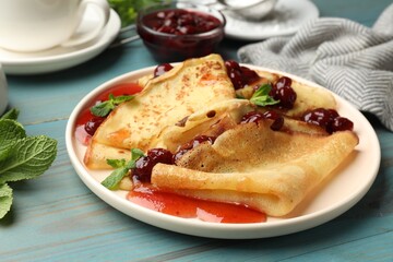 Delicious crepes served with cherry jam on light blue wooden table, closeup
