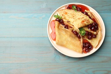 Delicious crepes served with cherry jam on light blue wooden table, top view. Space for text