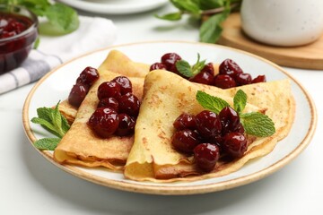 Delicious crepes served with cherry jam on white table, closeup