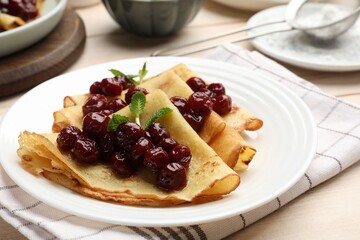 Tasty crepes with cherries and mint served on white wooden table, closeup