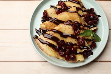Tasty crepes with cherries, chocolate and mint on white wooden table, top view