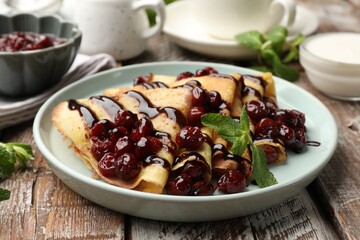Tasty crepes with cherries, chocolate and mint served on wooden table, closeup