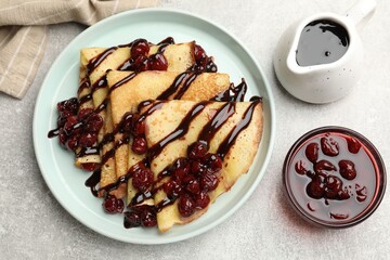 Tasty crepes with cherries and chocolate served on light table, flat lay