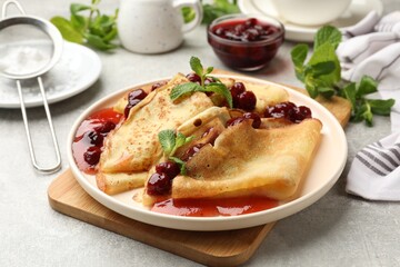 Tasty crepes with cherries, jam and mint served on light table, closeup