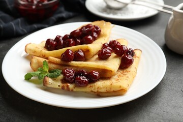 Tasty crepes with cherries, jam and mint served on black table, closeup