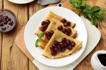 Tasty crepes with cherries and mint served on wooden table, flat lay