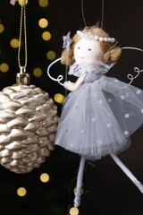 Obraz premium Beautiful Christmas bauble and fairy doll hanging against black background with blurred lights, closeup