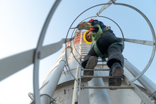 Industrial ladder climber on concrete and cement tower with safety equipment and harness under clear sky.