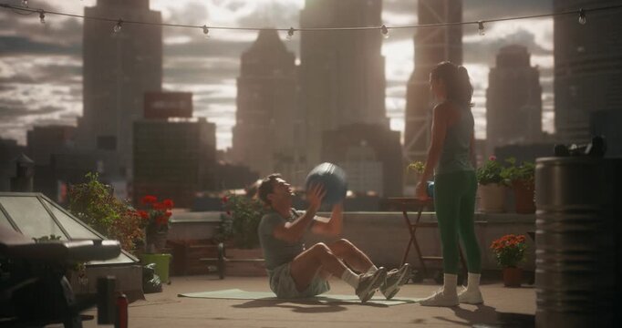 Man Performs Medicine Ball Sit Ups While a Young Woman Stands Nearby, Guiding the Throw and Catch on a Rooftop Workout Space, Focusing on Exercise, Core Strength, Health, and Calm Mindful Training.