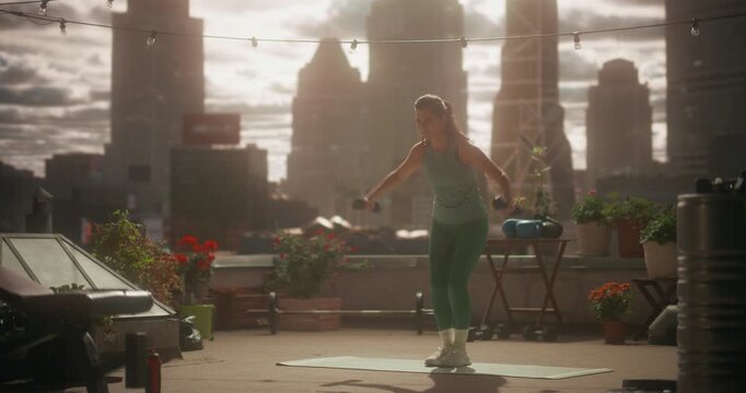 Woman Performs Dumbbell Lift and Side Raise on a Rooftop Mat, Using Home Exercise for Strength, Everyday Fitness, Health Care, and Calm Mindful Training in a Improvised Outdoor Workout Garden Gym 