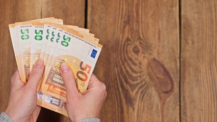 Top view of a woman counting euro banknotes with copy space on a wooden table on background, concept of finance, budgeting, savings, and cash management.