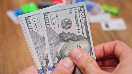 Woman counting US dollar bills with blurred credit cards in the background, representing finance, budgeting, spending, and cash management concepts.