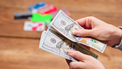 Woman counting US dollar bills, blurred credit cards in the background, symbolizing debt, loans, credit, financial illiteracy, and personal budgeting.