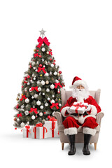 Santa claus sitting in armchair with a present in front of a Christmas tree