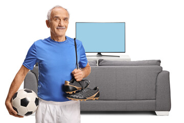 Elderly man with football equipment for training in front of a tv and sofa