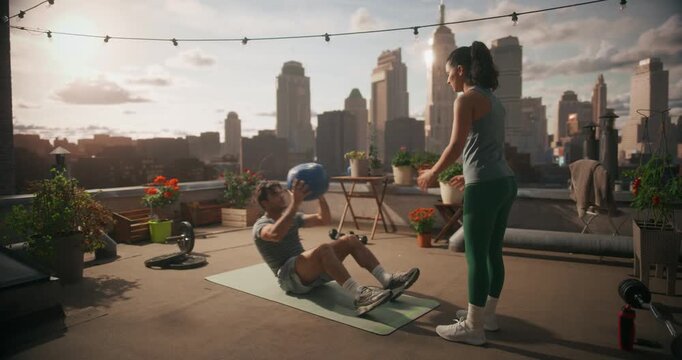 Young Man Performs Sit ups and Throwing Medicine Ball to Partner. Couple Exercises Together, Counting Reps, Correcting Form. Core Workout Together Outdoors Gym