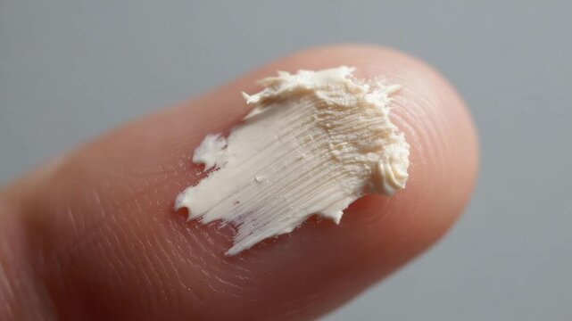A fingertip with a blob of white cream smeared on the nail.
