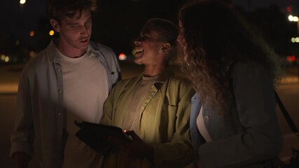 Three diverse friends using a tablet at night in the city - Powered by Adobe