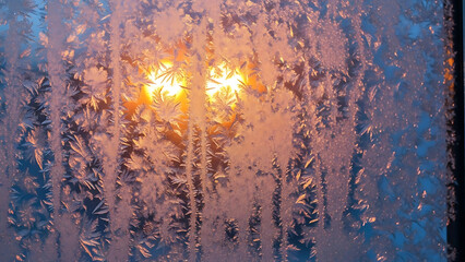Warm sunlight filters through a frosted windowpane creating a beautiful abstract pattern of ice crystals and vibrant orange and blue hues on a cold winter morning