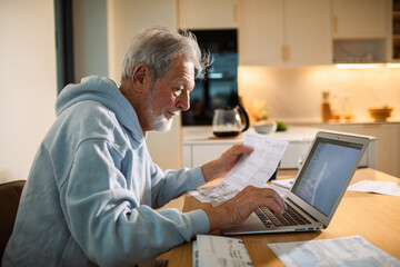 Senior man focused paying bills online at home kitchen table