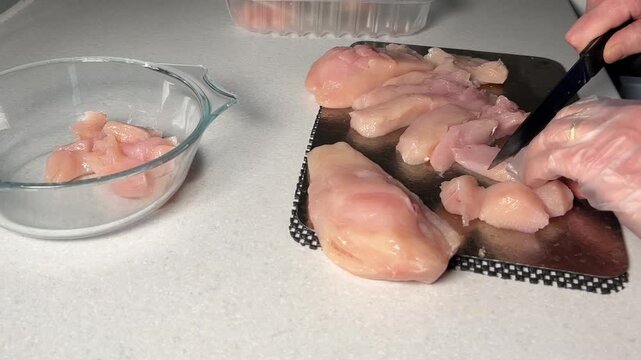 Female hands chopping up chicken on titanium board.