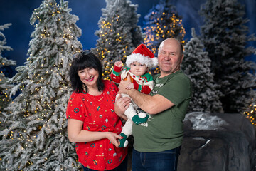 Grandparents posing with grandchild during festive Christmas. baby is dressed in Santa hat and holiday sweater, held lovingly by smiling grandparents. Snow-covered Christmas trees and warm twinkling 