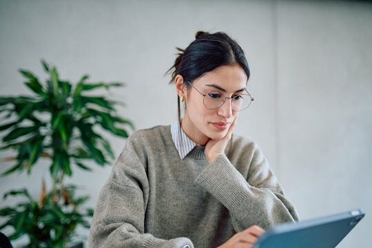 Young professional businesswoman focusing on her work, using a digital tablet in a casual office setting. Technology and productivity concept