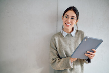 Young woman in glasses smiling, holding a tablet, looking thoughtfully to the side. Representing future vision and digital work
