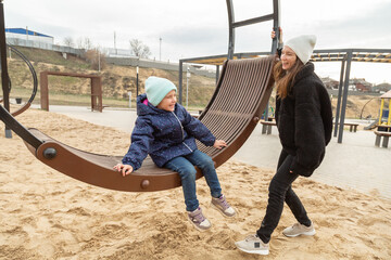 Family day. Happy girl swinging on swings having fun with mother on outdoor playground in park.