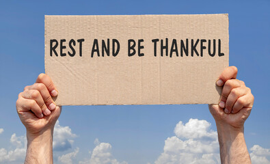 Hands holding a piece of cardboard with the inscription "Rest and be thankful"