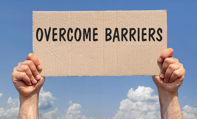 Hands holding a piece of cardboard with the inscription "Overcome barriers"