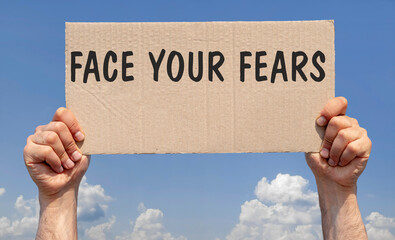 Hands holding a piece of cardboard with the inscription " Face your fears"