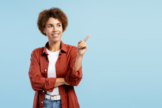 Happy young woman smiling while pointing up, showing direction on blue backdrop