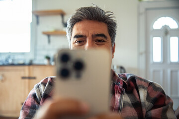 Mature man smiling while using smartphone at home