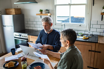 Mature couple focused on household finances at home kitchen