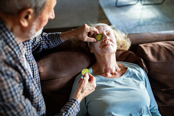 Senior husband pampering relaxed wife with face mask at home
