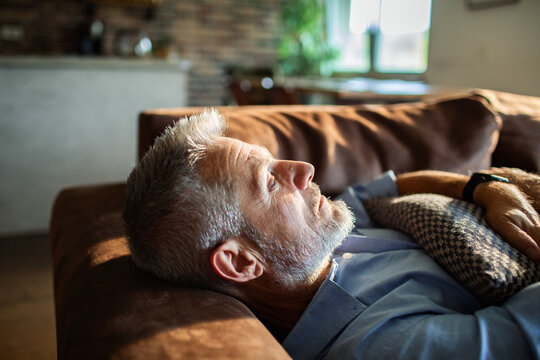Mature man resting thoughtfully on sofa at home