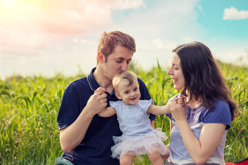 Happy family in the summer field on a sunny day. Mom and dad hold their little daughter in their arms