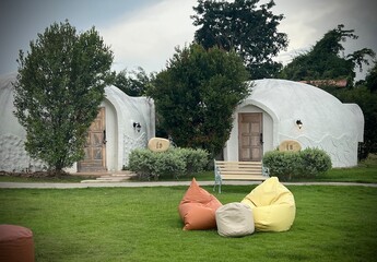 Ratchaburi, Thailand : Unique dome shaped resort among green tree, featuring a grassy lawn with colorful bean bags for relaxation at IGLOO Suanphueng resort.