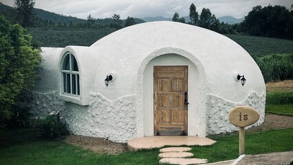Ratchaburi, Thailand :Beautiful architecture of white dome bungalow with arch window and door linked by a walkway on lush green lawn with mountain view at IGLOO Suanphueng resort. © Veruree