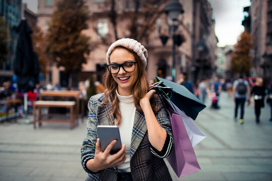 Young woman smiling and texting after shopping on city street
