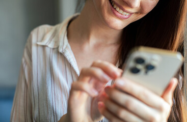 Young adult woman smiling while texting on smartphone at home