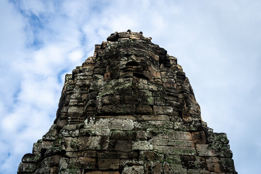 Ancient stone face of Bayon temple in Angkor, Cambodia, against a cloudy sky
