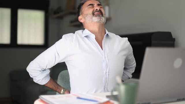 Mature businessman suffering from back pain at office desk