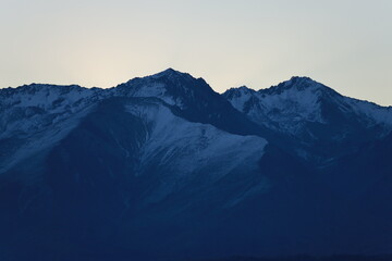 Lake Pukaki, NZ - May 24, 2025: A dramatic twilight close-up of dark, snow-dusted mountain peaks silhouetted against a pale sky. The rugged texture of the range is prominent.