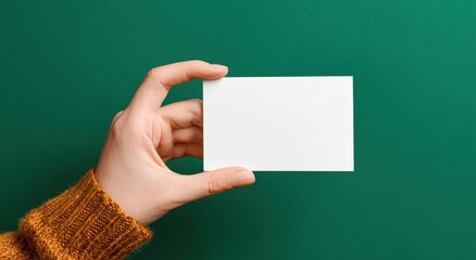 Hand holding a blank square card against a green background