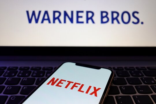 Salvador, Brazil - December 5, 2025: Netflix logo on smartphone screen and Warner Bros. logo in the laptop. Netflix and Warner Bros. 