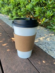 Morning coffee cup on wooden bench with sunlight and greenery