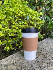 Hot takeaway coffee on bench by granite table and hedges