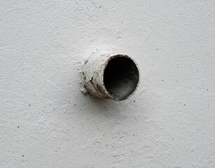 Concrete wall features a weathered pipe extending from its surface in a residential area during daylight